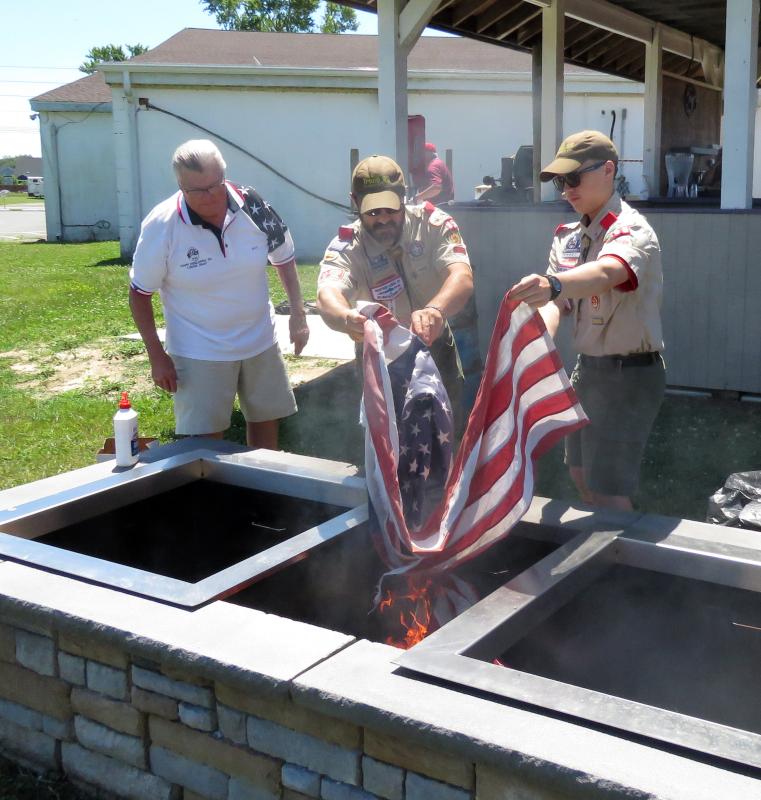 Mike Bradley of the Elks Flag Retirement Team watches Scout Leader Matt Teoli and son John of Boy Scout Troop 95 properly dispose of a used and faded flag in the specially designed Elks flag-burning pit.